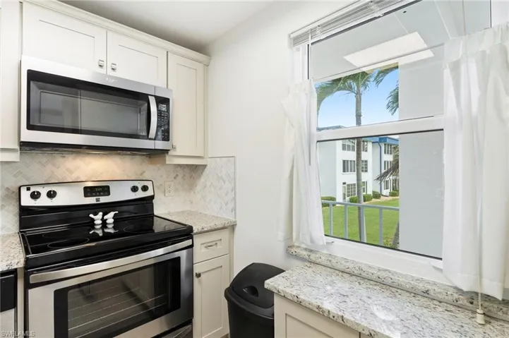 Kitchen with stainless steel appliances, light stone countertops, and a healthy amount of sunlight