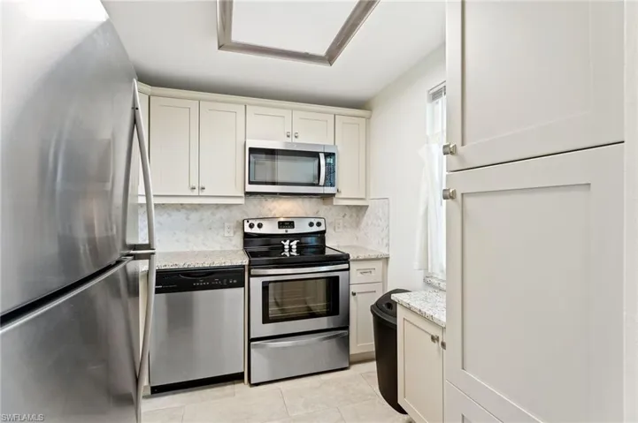 Kitchen with tasteful backsplash, light stone countertops, light tile patterned floors, and stainless steel appliances