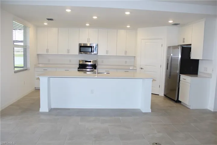 Kitchen featuring light countertops, a center island with sink, visible vents, white cabinets, and appliances with stainless steel finishes