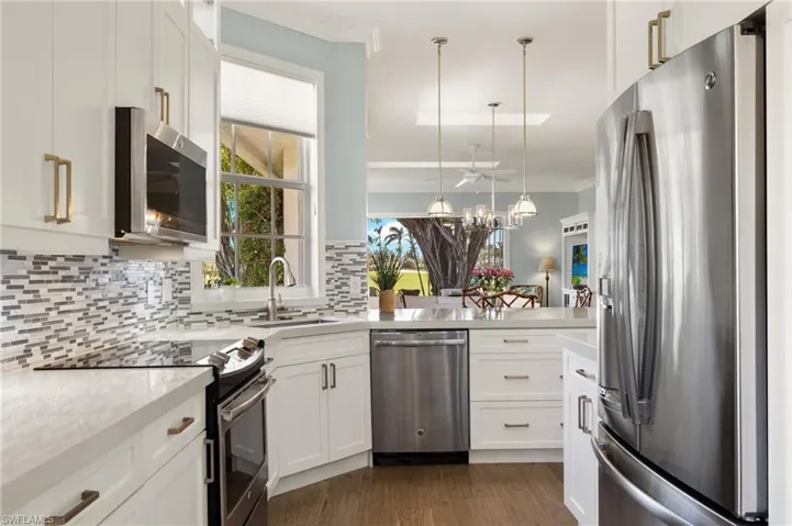 Kitchen with backsplash, white cabinets, hanging light fixtures, dark hardwood / wood-style floors, and stainless steel appliances