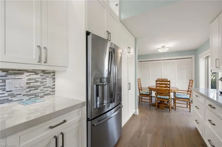 Kitchen with stainless steel refrigerator with ice dispenser, tasteful backsplash, light stone counters, white cabinets, and hardwood / wood-style floors