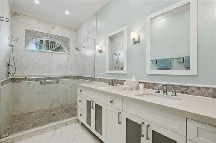 Bathroom with tiled shower, crown molding, vanity, and tile walls