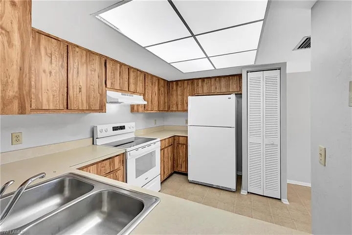 Kitchen featuring white appliances, light countertops, brown cabinets, under cabinet range hood, and light tile patterned flooring