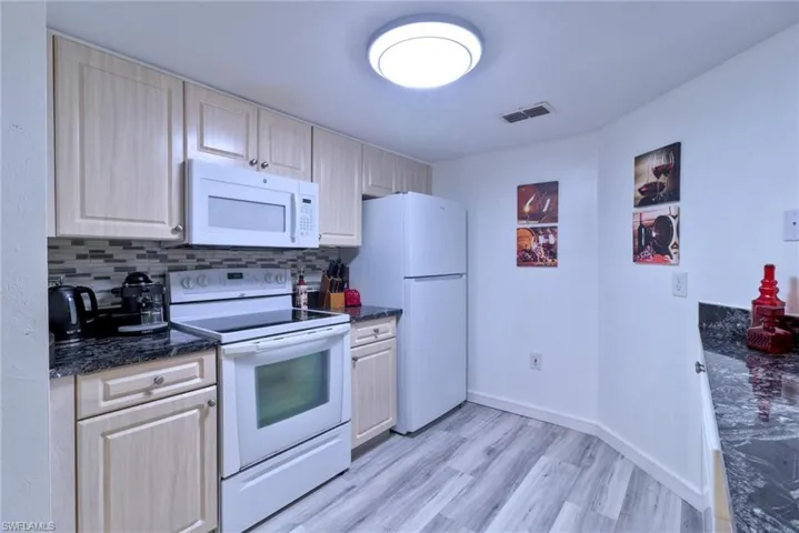 Kitchen with white appliances, light brown cabinets, dark stone countertops, decorative backsplash, and light wood-type flooring