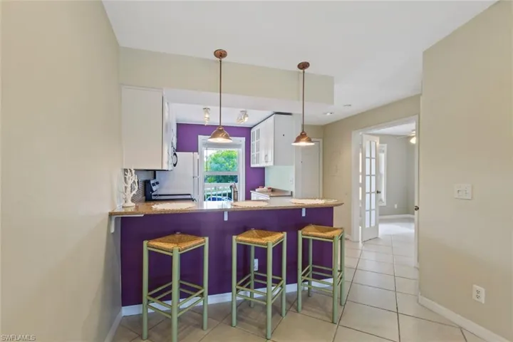 Kitchen featuring a kitchen bar, white cabinets, a peninsula, light tile patterned floors, and pendant lighting