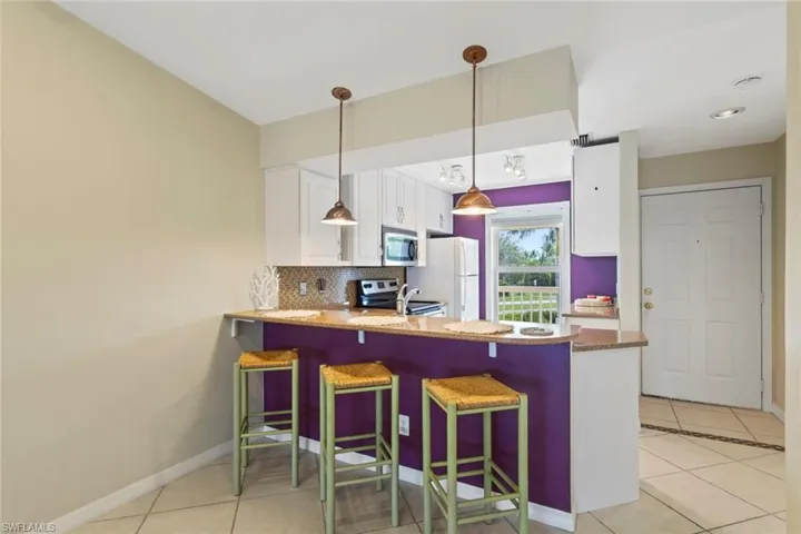 Kitchen with a breakfast bar area, light tile patterned floors, a peninsula, white cabinets, and backsplash