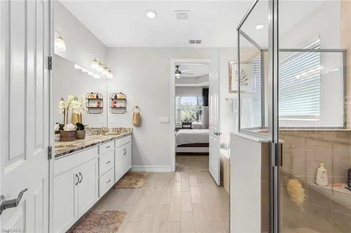 Bathroom featuring a dual vanity with a light-toned countertop, white cabinetry, and wood-finish flooring