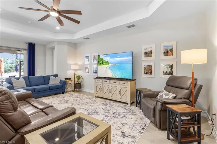 Spacious living area featuring light-toned walls, wood-finish flooring, and a tray ceiling with a ceiling fan
