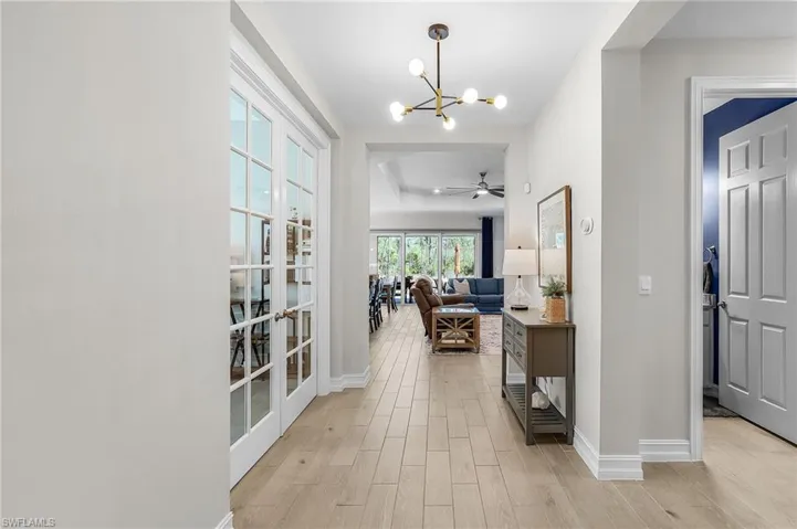 Bright hallway featuring wood-finish flooring, white baseboards, and a modern chandelier