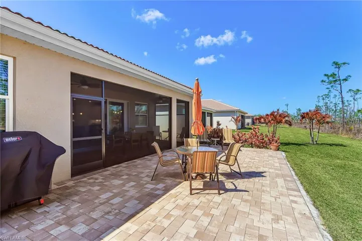 Spacious outdoor paver patio featuring a screened-in lanai, stucco exterior, and green lawn extending to natural landscaping