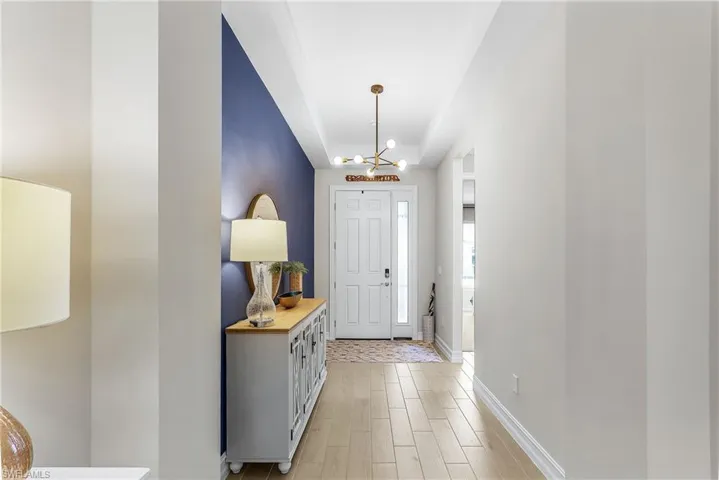 Inviting entryway featuring wood-finish flooring, a contemporary ceiling light fixture, a vibrant accent wall, and a paneled entry door with sidelights