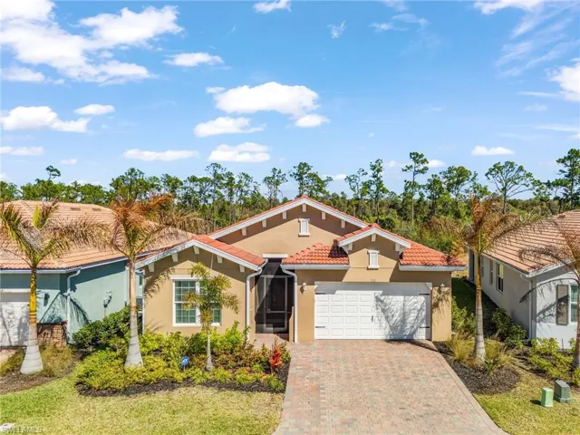 Stucco exterior with a tile roof, paver driveway, and an attached two-car garage