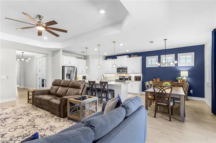 Open concept living area featuring a tray ceiling, wood-finish flooring, a kitchen with white cabinetry and stainless steel appliances, a kitchen island with seating, and a dining area