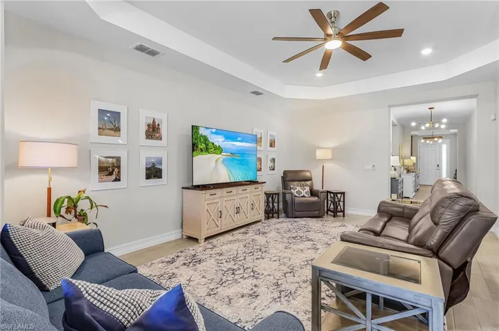 Spacious room featuring light wood-finish flooring, a tray ceiling with recessed lighting, and a modern ceiling fan