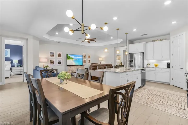 Open-concept living space featuring wood-finish flooring, a tray ceiling with recessed lighting, and a modern chandelier