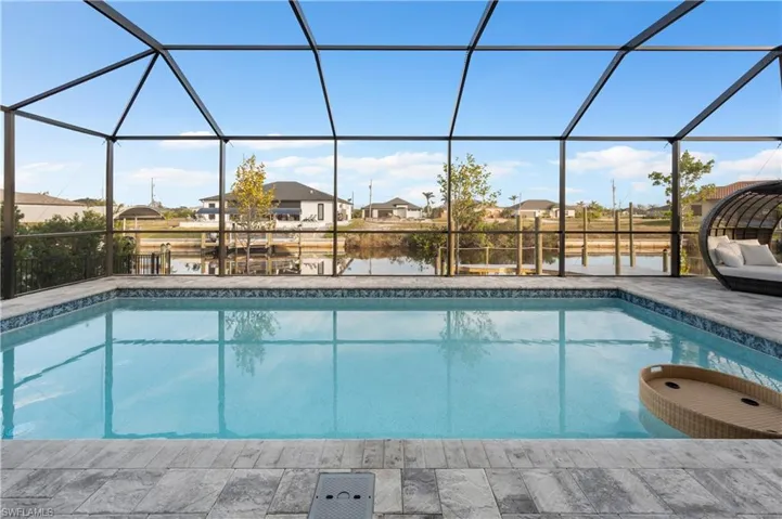 View of swimming pool featuring glass enclosure, a water view, and a patio