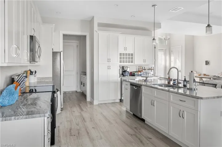 Kitchen with sink, decorative light fixtures, a kitchen island with sink, white cabinets, and appliances with stainless steel finishes