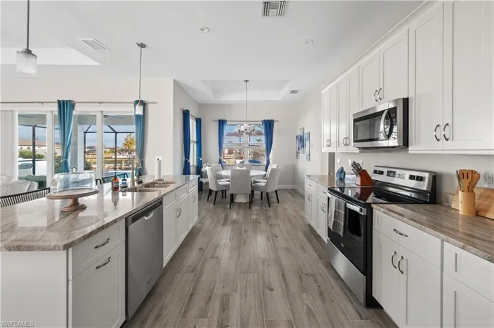 Kitchen with stainless steel appliances, a raised ceiling, sink, white cabinetry, and hanging light fixtures