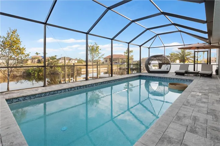 View of pool featuring glass enclosure, a water view, and a patio