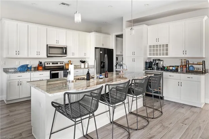 Kitchen featuring hanging light fixtures, light stone counters, a center island with sink, white cabinets, and appliances with stainless steel finishes