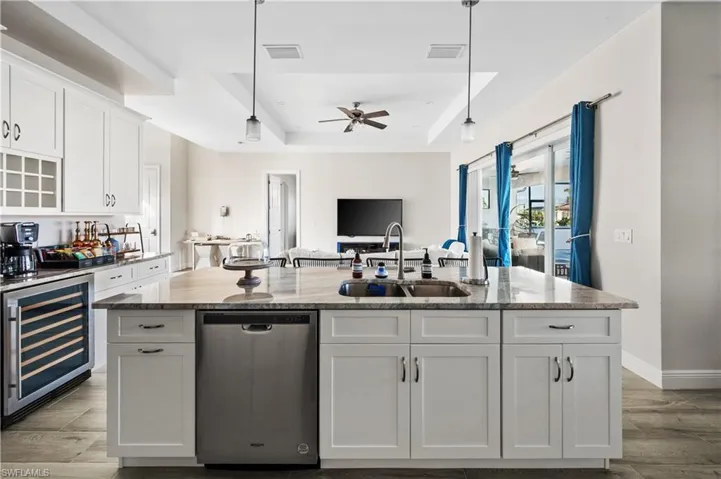 Kitchen with stainless steel dishwasher, sink, a kitchen island with sink, and beverage cooler