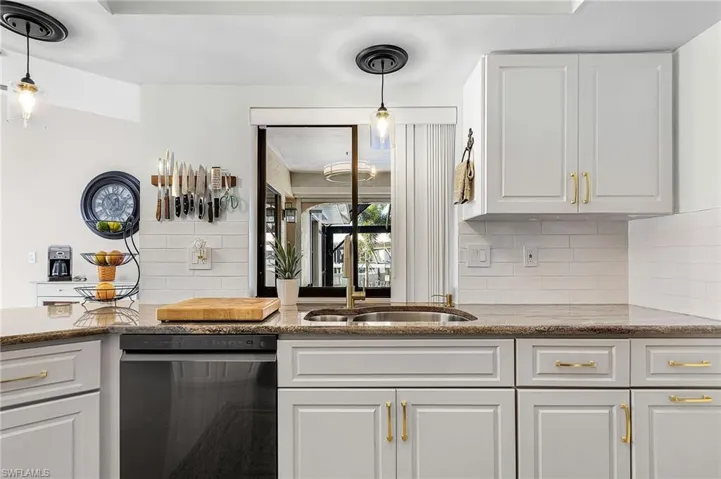 Kitchen with white cabinets, decorative backsplash, stainless steel dishwasher, light stone counters, and hanging light fixtures