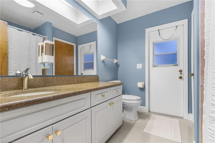 Bathroom with a shower with shower curtain, light tile patterned flooring, vanity, and a skylight