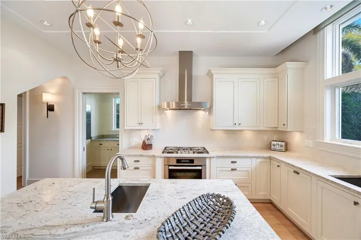 Kitchen featuring light stone countertops, stainless steel appliances, hanging lights, light wood-style flooring, and decorative backsplash