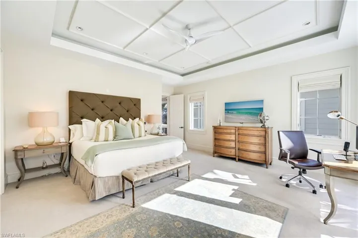 Bedroom with light colored carpet, a tray ceiling, and an office area