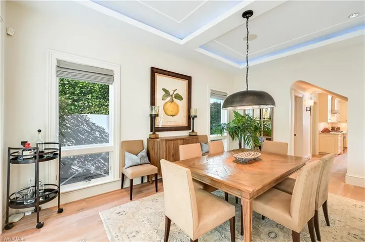 Dining space featuring arched walkways, light wood finished floors, and a raised ceiling