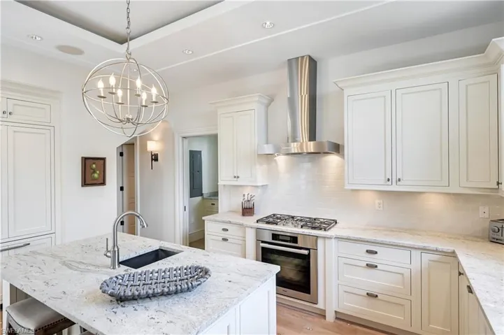 Kitchen with light stone countertops, stainless steel appliances, white cabinetry, an island with sink, and backsplash