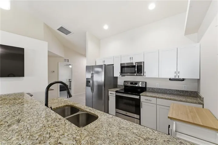 Kitchen featuring stainless steel appliances, lofted ceiling, light stone countertops, and white cabinetry