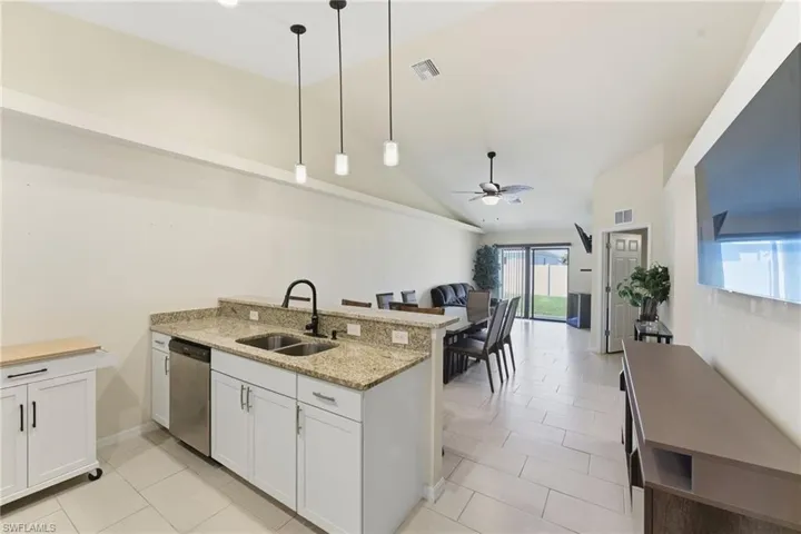 Kitchen with white cabinetry, ceiling fan, pendant lighting, light stone countertops, and vaulted ceiling