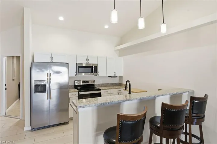 Kitchen featuring stainless steel appliances, decorative light fixtures, light stone countertops, white cabinetry, and vaulted ceiling
