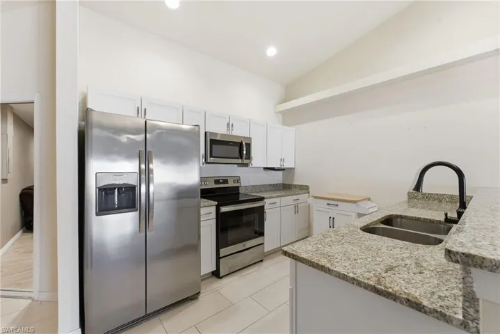 Kitchen featuring stainless steel appliances, vaulted ceiling, light stone countertops, white cabinets, and light tile patterned floors