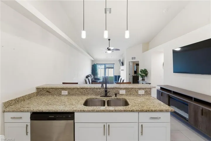 Kitchen with white cabinets, light stone counters, pendant lighting, stainless steel dishwasher, and vaulted ceiling