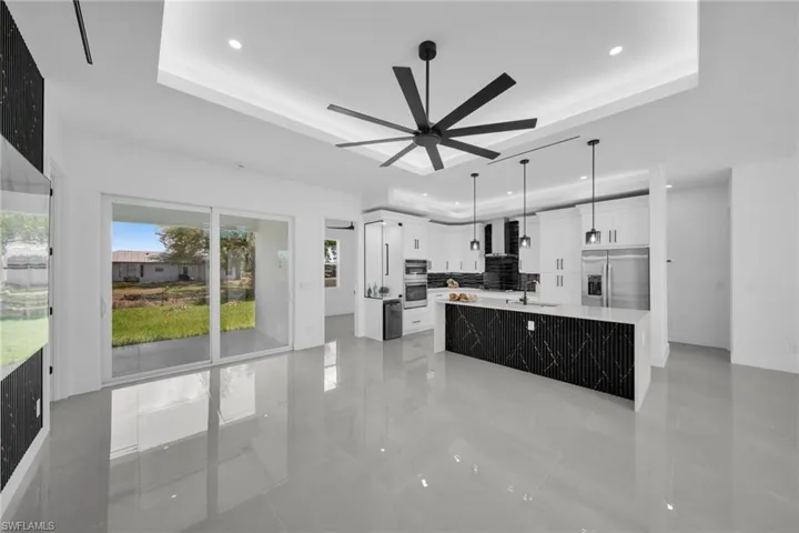 Kitchen with white cabinets, a large island, stainless steel appliances, hanging light fixtures, and light stone counters