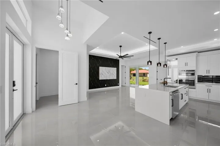 Kitchen with white cabinets, an island with sink, a tray ceiling, hanging light fixtures, and light stone counters
