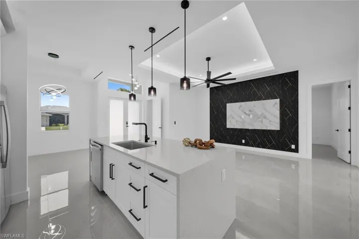 Kitchen featuring an accent wall, white cabinetry, a raised ceiling, a center island with sink, and light stone countertops