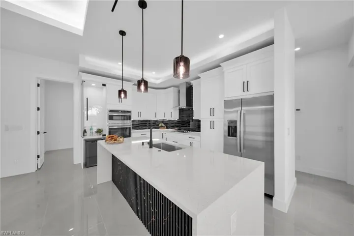 Kitchen featuring light stone countertops, stainless steel appliances, a center island with sink, backsplash, and white cabinets