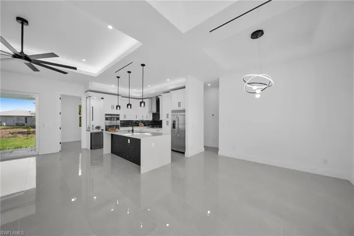 Kitchen featuring an island with sink, decorative light fixtures, white cabinets, light stone counters, and open floor plan