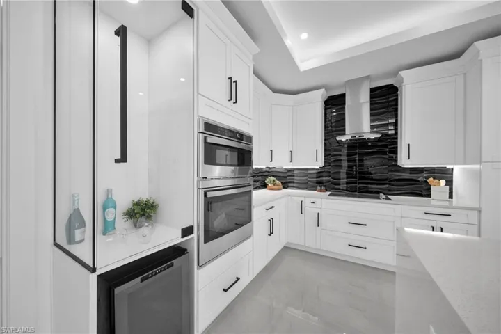 Kitchen featuring white cabinets, double oven, backsplash, light stone countertops, and recessed lighting