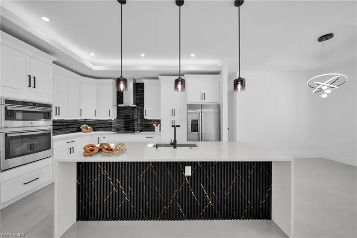 Kitchen with stainless steel appliances, backsplash, white cabinetry, a large island with sink, and light stone countertops