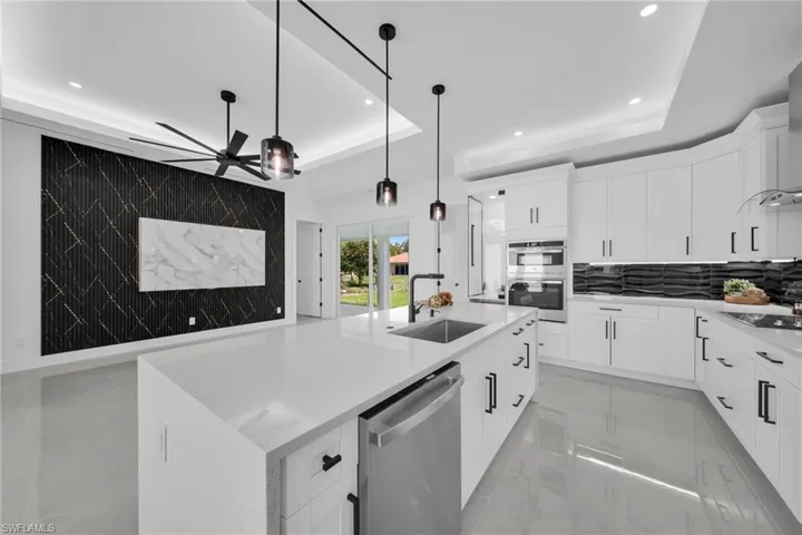 Kitchen featuring a tray ceiling, light stone countertops, stainless steel appliances, a center island with sink, and white cabinets