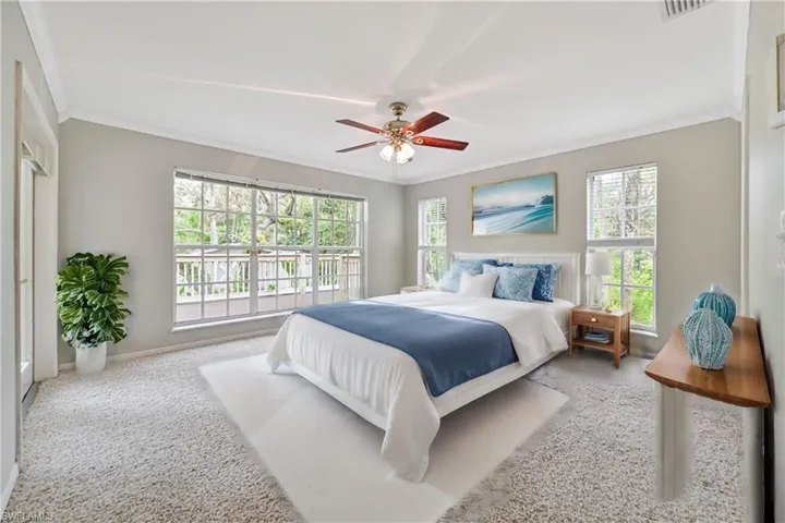 Carpeted bedroom featuring multiple windows, ceiling fan, and ornamental molding
