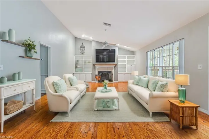 Living room with lofted ceiling, a fireplace, ceiling fan, and wood-type flooring