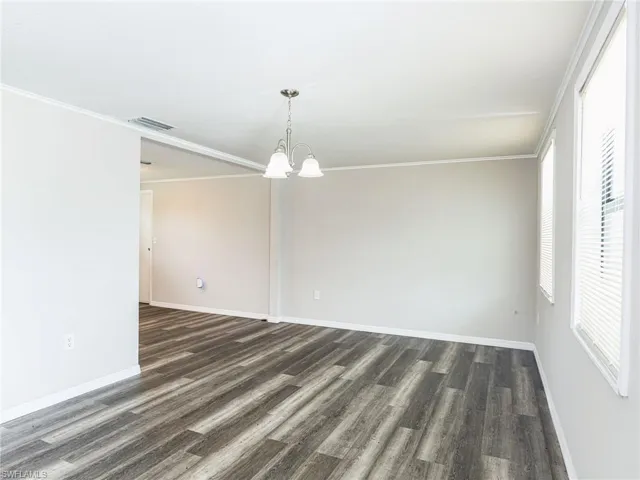 Spacious room featuring wood-finish flooring, light grey walls, white trim, and a brushed nickel chandelier with frosted glass shades