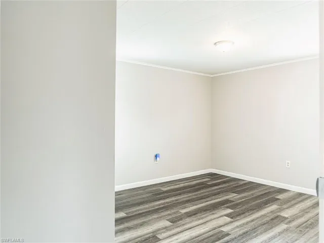 Neutral-toned interior room featuring wood-finish flooring, white baseboards, and crown molding
