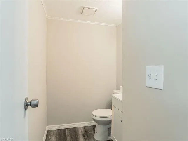 Bathroom with wood-finish flooring, light gray walls, white baseboards, and a white toilet
