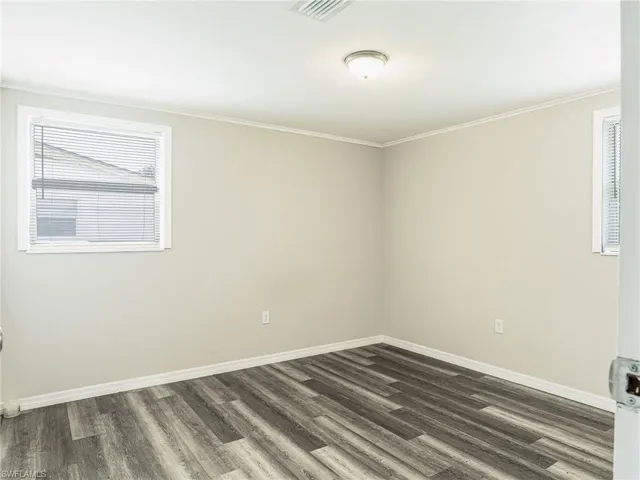 Room with wood-finish flooring, two windows with blinds, and a ceiling light fixture
